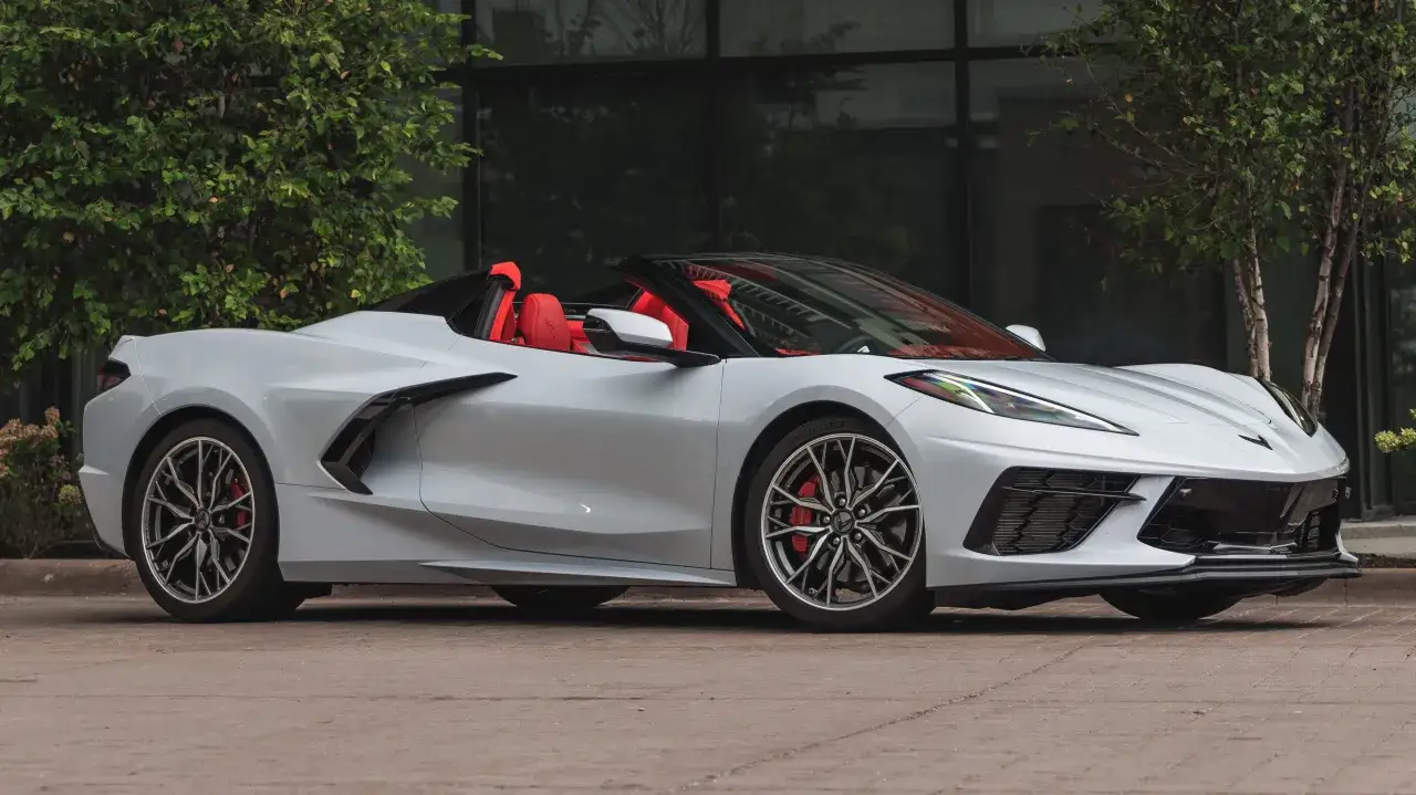 Srebrny roadster z czerwonym wnętrzem, zaparkowany przed budynkiem z zielenią.