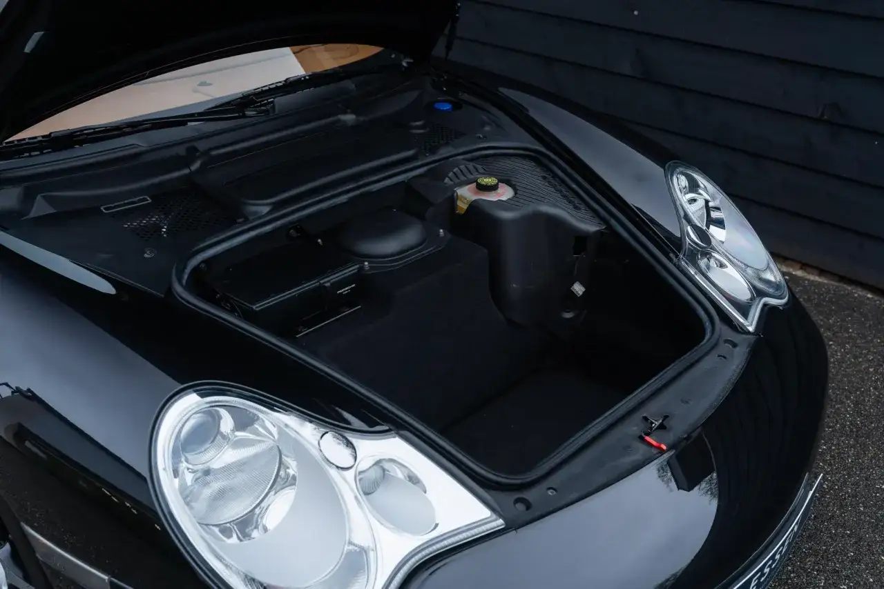 Przednia przestrzeń bagażowa czarnego Porsche 996, z widocznymi reflektorami i elementami komory silnika.