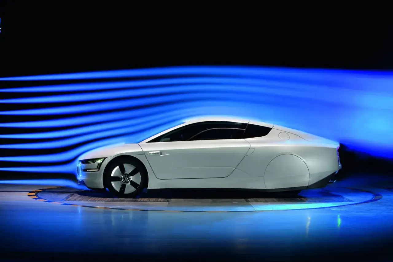 Biały, aerodynamiczny vw xl1 w tunelu aerodynamicznym, z niebieskimi smugami powietrza podkreślającymi jego kształt.