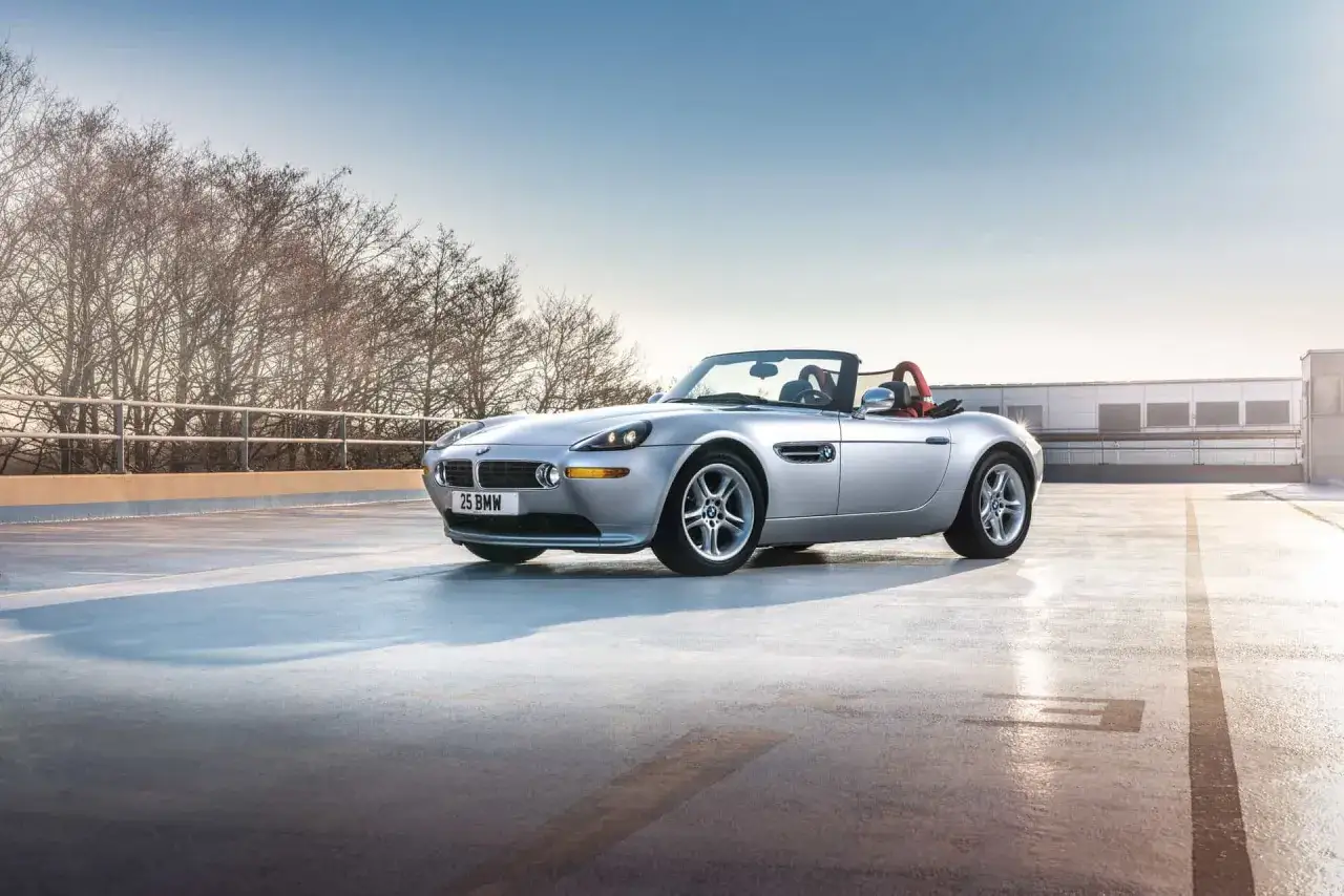 Srebrny kabriolet BMW Z8 z czerwonym wnętrzem zaparkowany na dachu parkingu, z drzewami w tle.
