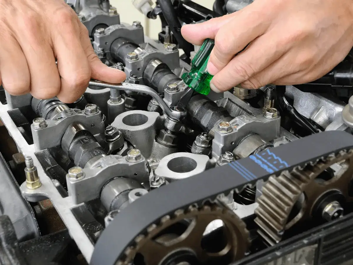 Mechanik reguluje luzy zaworowe silnika, używając klucza i śrubokręta.