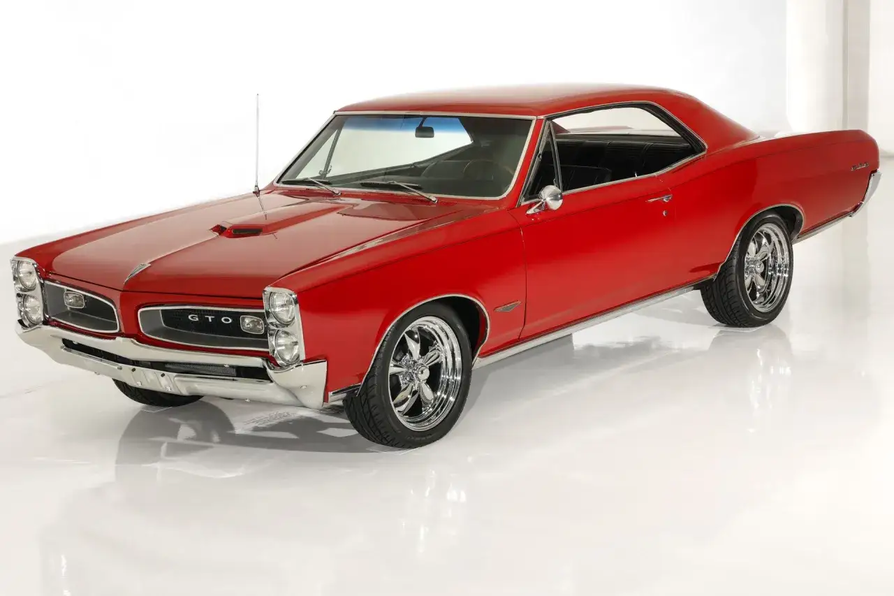 Klasyczny, czerwony Pontiac GTO z chromowanymi felgami, lśniącym lakierem i charakterystycznym wlotem powietrza na masce.