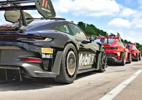 Czarny Porsche GT3 RS z numerem 3 i logo Manthey na skrzydle, gotowy do wyścigu obok czerwonych samochodów.
