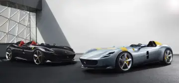 Dwa sportowe samochody Ferrari Monza SP2, jeden czarny, drugi błękitny z żółtymi pasami, prezentują swoje aerodynamiczne kształty.