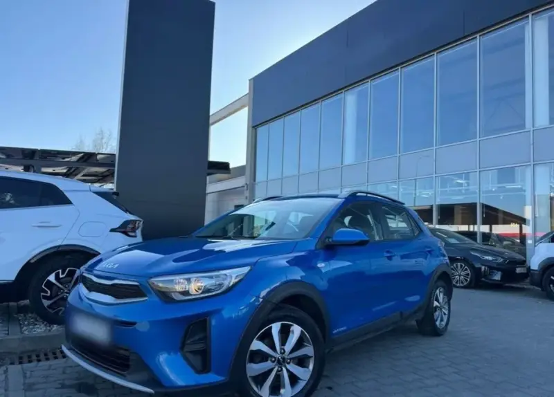 Błękitny Kia Stonic 2023 zaparkowany przed salonem samochodowym. Obok stoi biały SUV.