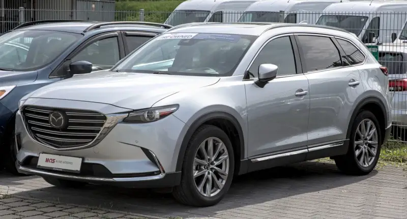 Srebrna Mazda CX-9 z napisem "PRE-OWNED" na przedniej szybie, zaparkowana na zewnątrz.