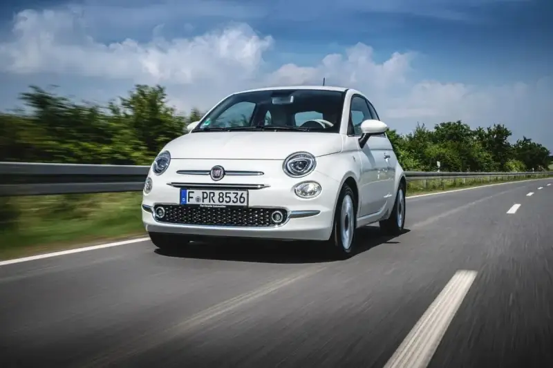 Biały Fiat Panda 3 jedzie po drodze, otoczony zielenią i błękitnym niebem.