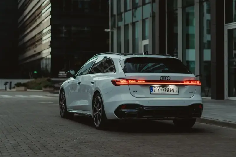 Białe Audi A5 Avant z nowoczesnymi światłami LED na tle miejskiej architektury.