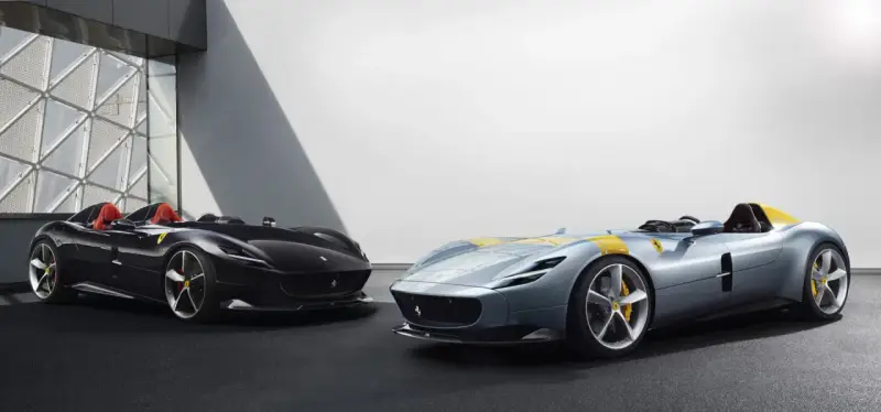 Dwa sportowe samochody Ferrari Monza SP2, jeden czarny, drugi błękitny z żółtymi pasami, prezentują swoje aerodynamiczne kształty.