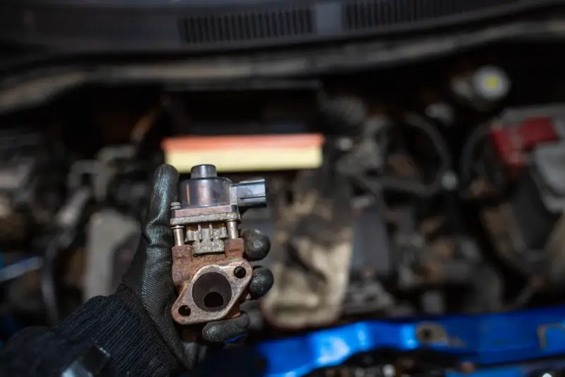Zardzewiały zawór EGR w dłoni mechanika. Może to być przyczyna problemów z silnikiem, np. nierównej pracy.