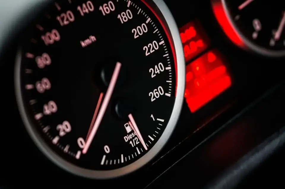 Zbliżenie na deskę rozdzielczą samochodu: prędkościomierz pokazuje 80 km/h, a obok wskaźnik paliwa jest na 1/2. Widoczny jest również licznik spalania paliwa.